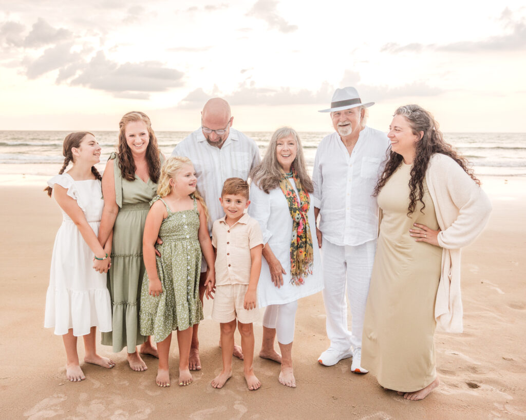 Family smiling together at sunrise on New Smyrna Beach with pastel sky in the background