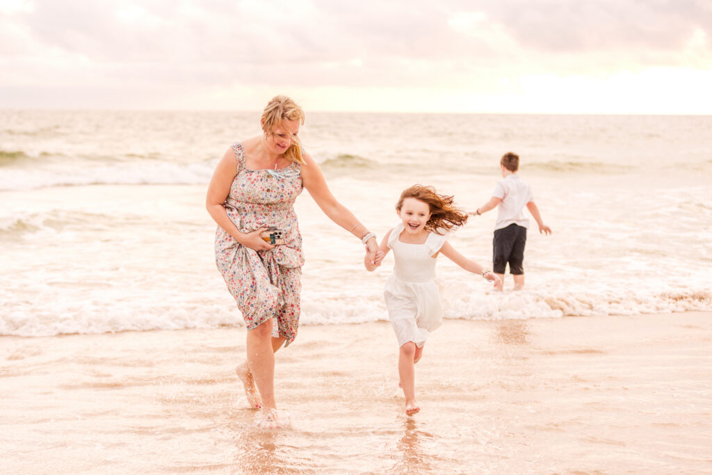 The best sessions are the ones where something bigger is happening under the surface. This extended family sunrise gender reveal session at New Smyrna Beach was exactly that — a whole crew showing up at the crack of dawn, some of them not yet knowing why. Fun doesn't quite cover it.
If you're curious about how I run mornings like this on the beach, you can check out my session details — but here's the honest version of how this one actually went.

This session started with wind. Not a gentle breeze — actual, hair-everywhere, try-to-hold-your-dress-down wind. The sky was overcast when we kicked things off, which honestly wasn't the worst thing. Soft light, no one squinting, and a moody backdrop that made the early shots feel a little cinematic. Then the sun pushed through and the whole beach lit up, right on cue like it knew what was about to happen.
The family was loose and easy from the start. Extended family sessions can go sideways fast — too many people, too many opinions, someone's always wandering off — but this group was genuinely just happy to be there. The excitement of the pregnancy announcement and gender reveal was doing all the heavy lifting. Candid moments were everywhere. I barely had to prompt anyone.
